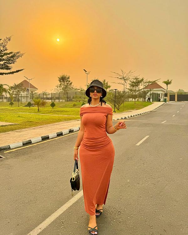Regina Daniels in Rust Off-Shoulder Maxi Dress & Bucket Hat at Sunset | OutfitLibrary.com